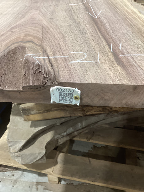 A walnut wood slab with a QR tag attached to it, placed among other slabs, with markings on the wood surface.