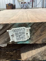 A close-up image of a walnut slab edge with a QR code attached.
