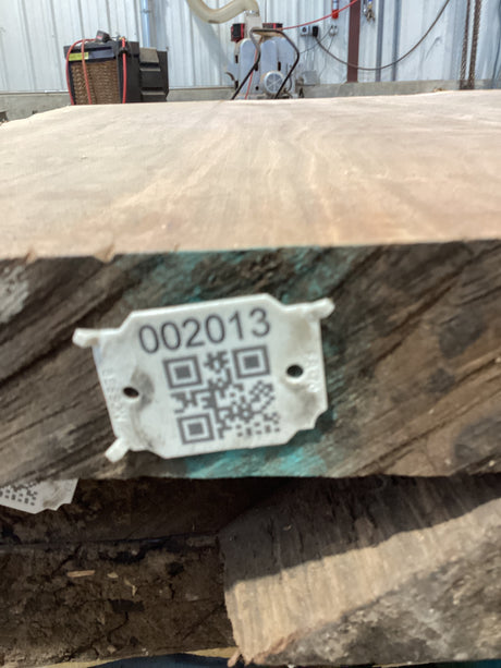 A close-up image of a walnut slab edge with a QR code attached.