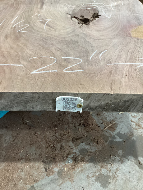 A walnut slab with a distinct live edge, markings on the surface, and a visible QR label in the lower part of the image.