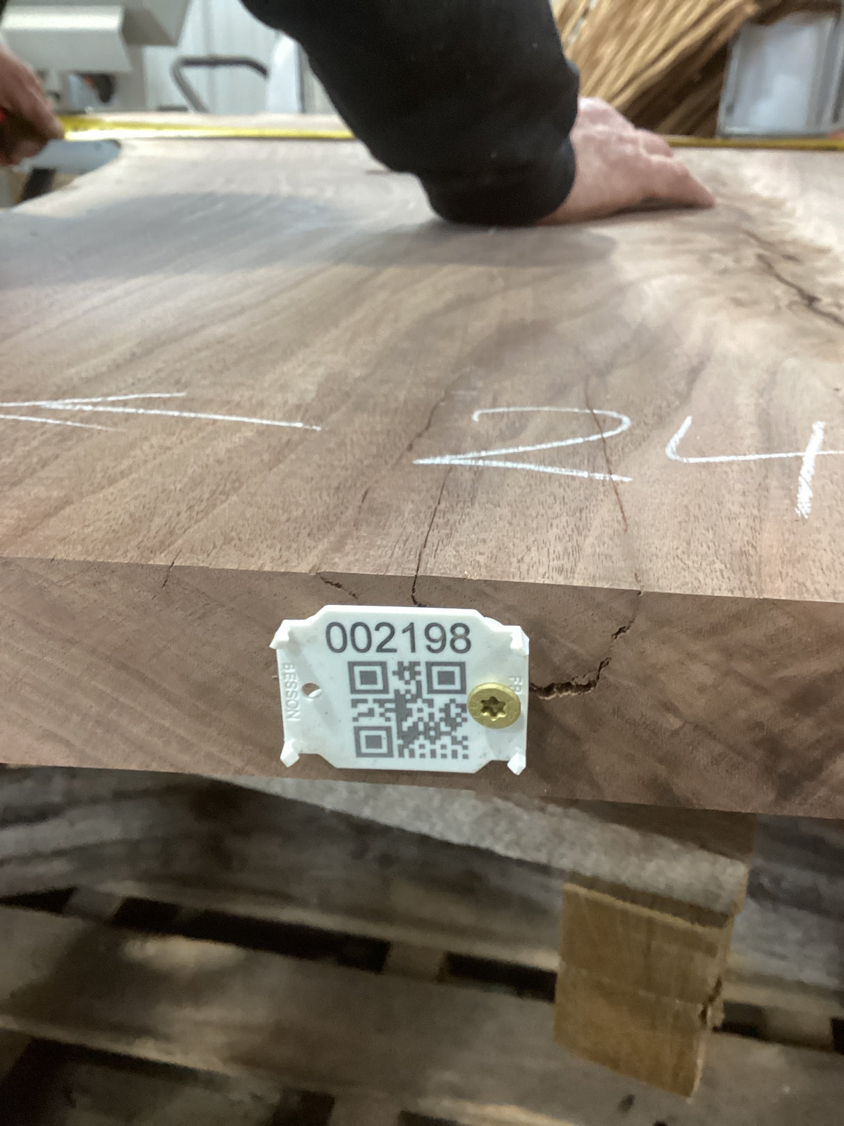 A walnut slab with a unique crotch wood figure, marked with white lines and a tag containing a QR code and number.