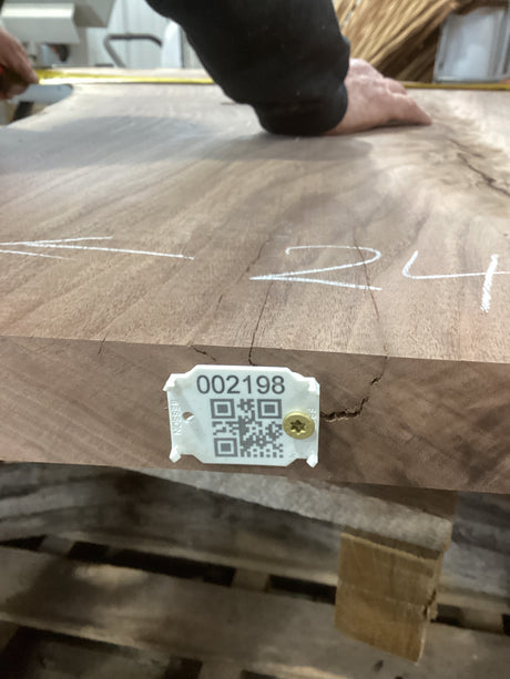 A walnut slab with a unique crotch wood figure, marked with white lines and a tag containing a QR code and number.