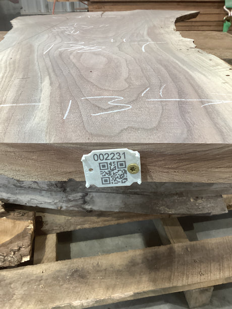 A walnut slab with visible wood grain patterns, marked with a measurement tape and a QR code tag.