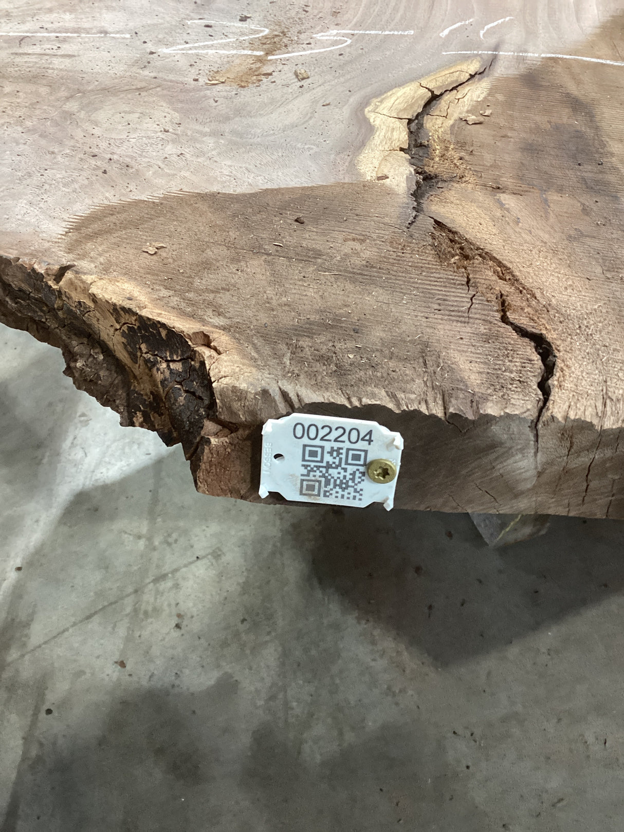 A rough walnut wood slab with a visible wood grain and a few cracks, tagged with a QR label.
