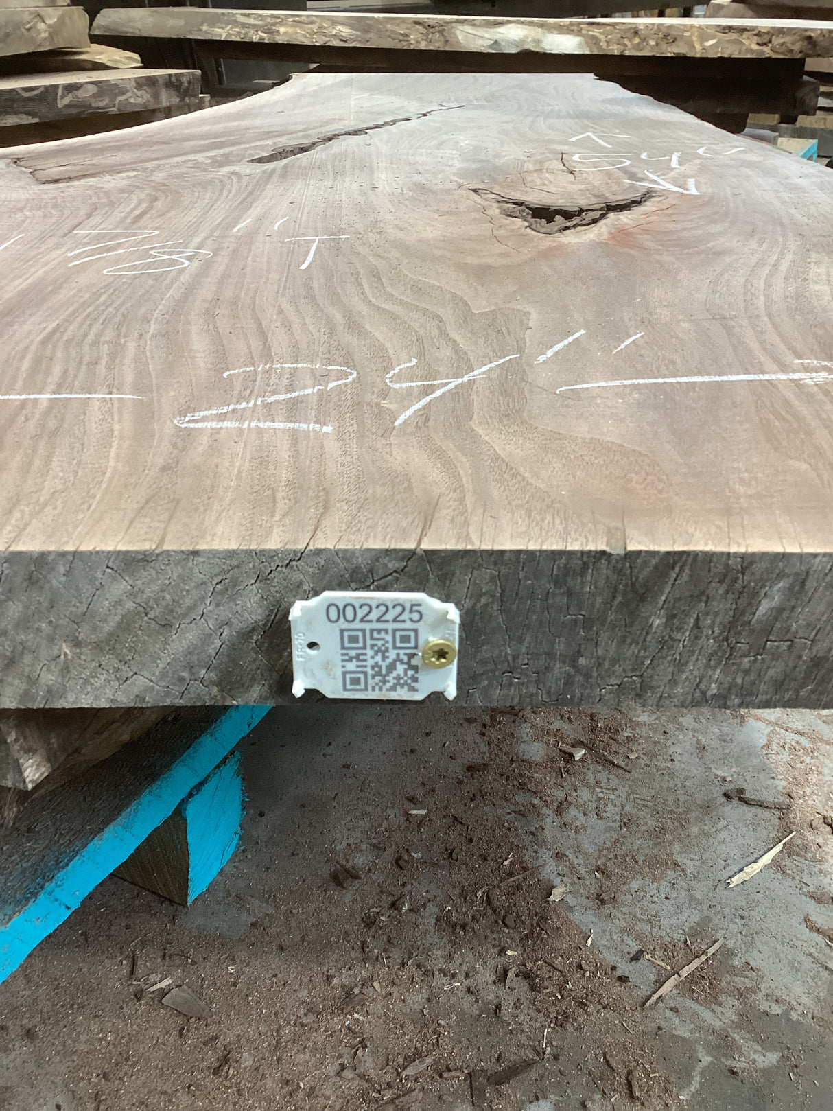 A walnut wood slab with visible knots and natural edge, bearing a label with a QR code.