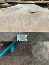 A walnut wood slab with visible knots and natural edge, bearing a label with a QR code.
