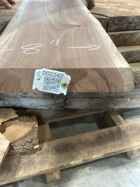 A walnut slab with a visible wood grain pattern and a QR tag attached to it, placed on a wooden rack.
