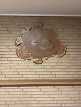 A circular wooden wall hanging art piece with a rustic finish mounted on a brick wall.