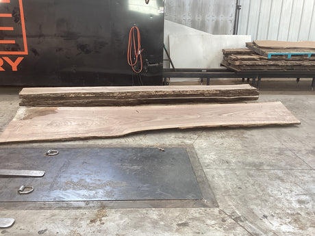 Pieces of large walnut slabs stacked up on top of each other on a concrete floor.