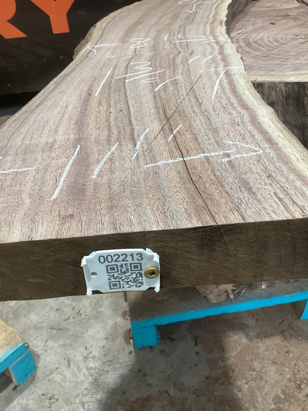 A walnut wood slab with visible growth rings and a cut edge, marked by white lines and a QR tag.