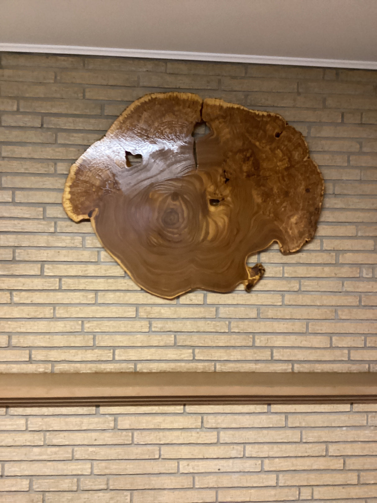 A circular wooden wall hanging art piece with a rustic finish mounted on a brick wall.