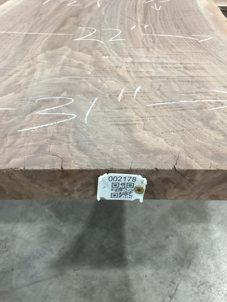 A walnut slab with visible measurements marked on it, indicating it has been cut or processed for furniture making. QR label attached to the edge of the slab.
