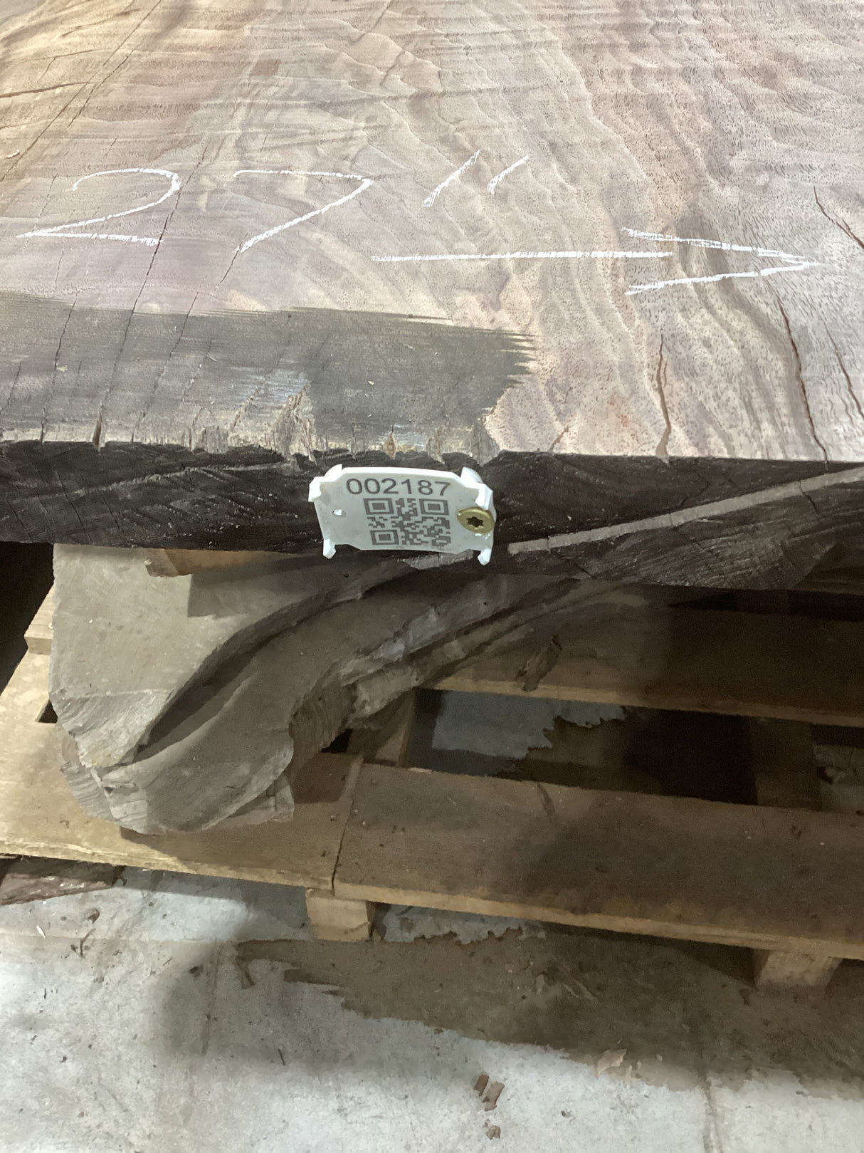 A walnut slab with visible live edge contours and natural wood patterns, placed on a pallet with a QR label on the edge.