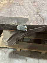 A walnut slab with visible live edge contours and natural wood patterns, placed on a pallet with a QR label on the edge.