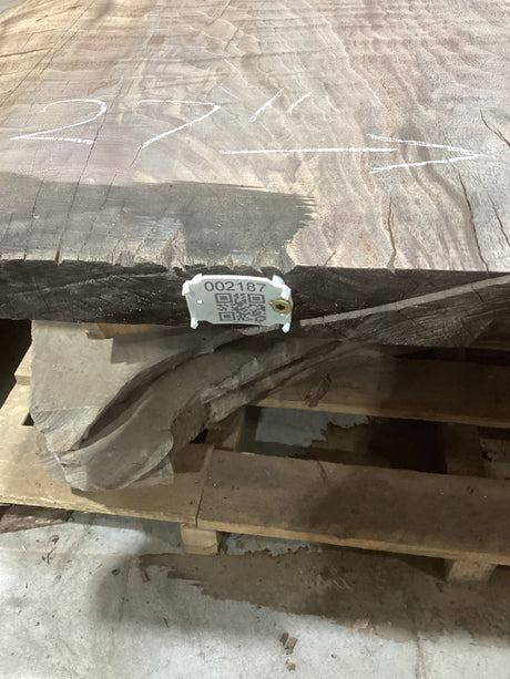 A walnut slab with visible live edge contours and natural wood patterns, placed on a pallet with a QR label on the edge.