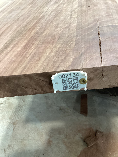A walnut wood slab with a visible grain pattern and a tag attached to it showing a QR code and a number.
