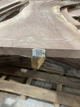 A walnut slab with natural color variations and a visible QR label attached to it, placed on a wooden pallet.