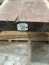 A walnut slab with a visible wood grain pattern and a QR tag attached to it, placed on a wooden pallet.
