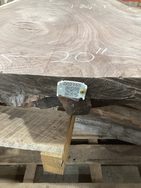 An irregularly shaped walnut slab with a distinctive striped figure pattern, resting on a wooden support with a visible QR label.