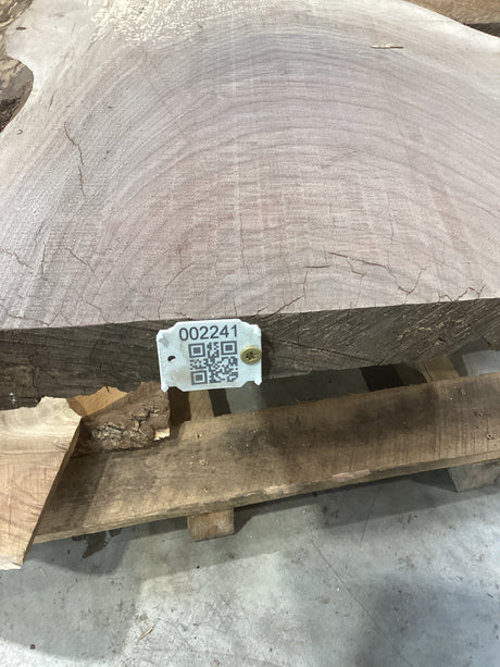 A walnut slabresting on a wooden support, with a tag attached that includes a QR code.