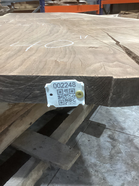 A walnut slab edge with a tag attached to it, displaying a QR code and an identification number.