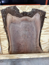 A close-up image of a walnut slab with a tiger-striped figure, indicating the natural grain of the wood. Against a plywood background.
