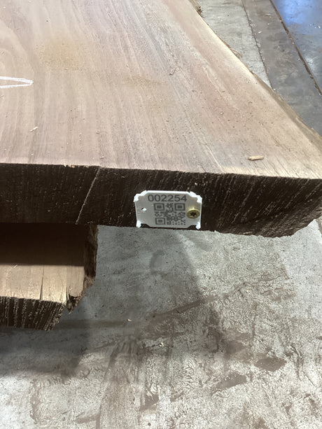 A walnut slab with a live edge, displaying unique figure and grain patterns, marked with a QR tag indicating its sku.