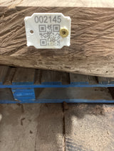 A walnut wood slab with a visible figure, placed on a blue pallet, with a tag attached to it showing a QR code and product information.