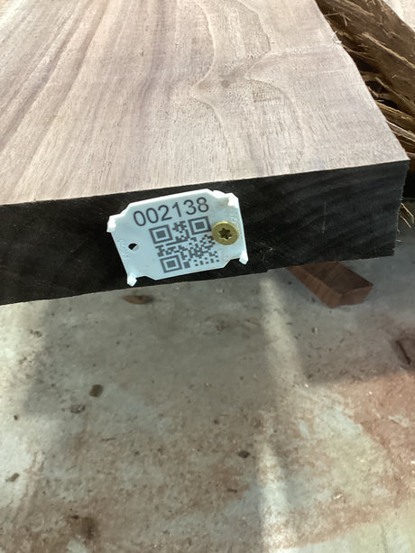 A walnut slab with a visible QR code and a number tag attached to it, likely indicating a product identification or inventory control system.