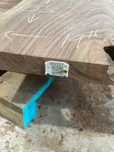 A walnut wood slab with a live edge feature, marked with white lines and a QR label.