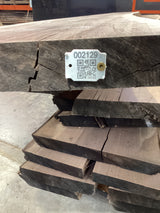 A walnut wood slab with a visible QR code on a tag attached to it, placed among other slabs.