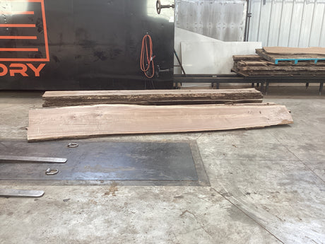 Large walnut wood slab propped against other wood slabs on concrete floor.